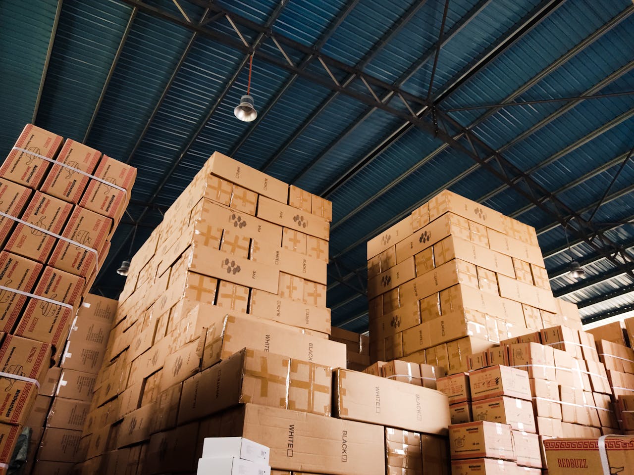 services-03 High stacks of cardboard boxes organized in a warehouse with a blue metal ceiling.